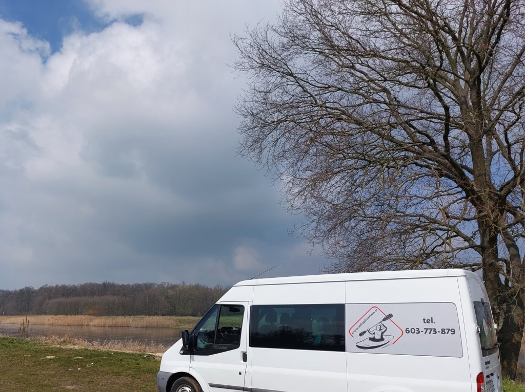 widok firmowego wana przed rzeką z drzewem po prawej stronie